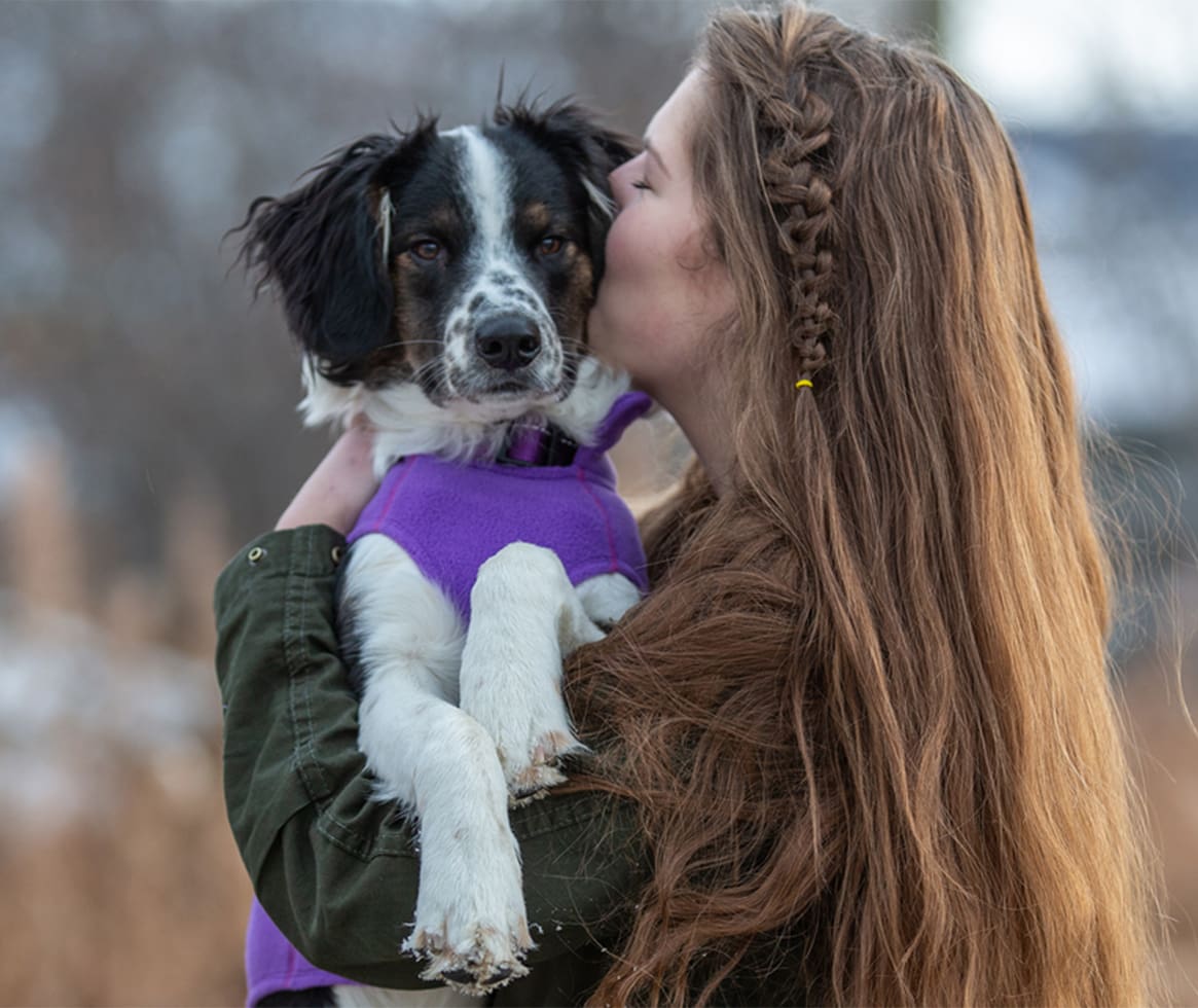 Woman kissing dog in purple fleece